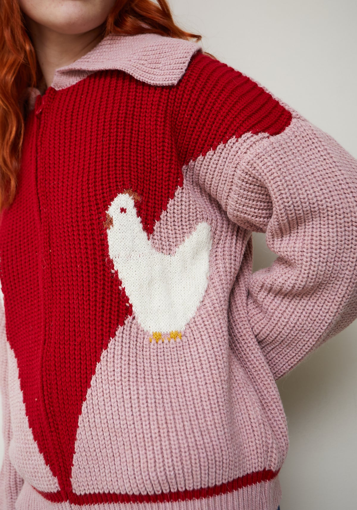 Detalle del cárdigan Farm rosa y rojo, con gallina blanca de patas amarillas, textura de punto grueso y cuello rosa empolvado.